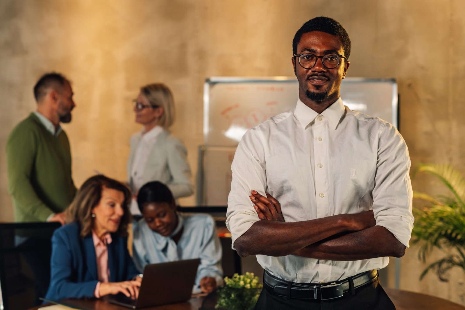 Portrait of elegant african american leader standing at conference room with arms crossed and smiling at the camera on a meeting of his team. Confident professional businessman posing at boardroom.
