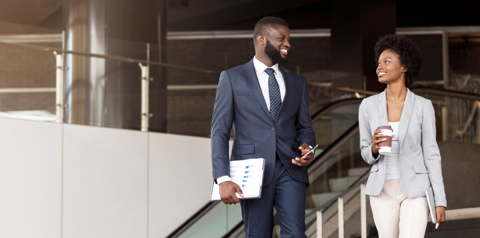 Two cheerful african american employees leaving office building for coffee break, panorama with copy space